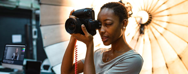 A photographer holds a camera and puts their eye to the viewfinder.