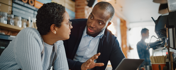 A woman and a man converse while huddled over a laptop in a cafe.