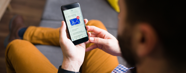 Person holding a smartphone displaying an email notification while sitting on a couch.